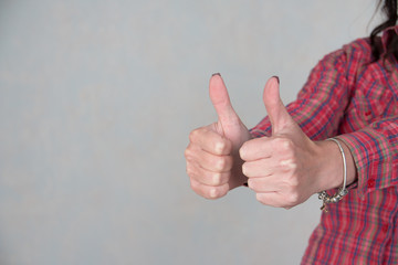 woman showing thumbs up sign in office with copy space.girl dressed in casual clothing. Focus at hands. she giving thumb up as sign of success on gray background. customers feedback concept