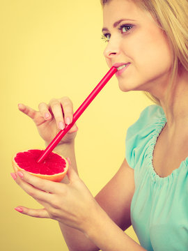 Woman drinking juice from fruit, red grapefruit