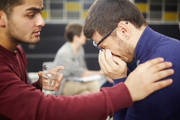 Young man crying and wiping tears with handkerchief while groupmate supporting him