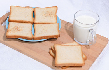 Square toast on a blue plate on a wooden board and a mug of milk