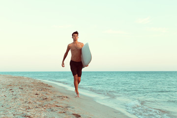 Fototapeta na wymiar Handsome surfer holding his surfboard