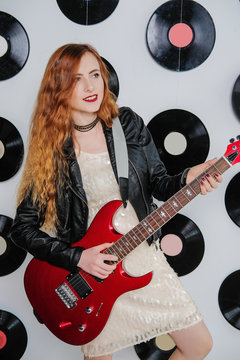 Sexy woman in a sequin dress, leather jacket and red lips. Disco style. Girl hipster playing the guitar.