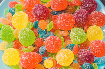 Bright colored candy, marmalade, sweets in a blue plate on a dark background top view