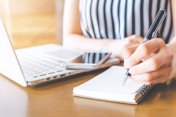 Business woman hand working at a computer and writing on a noteped with a pen in the office.
