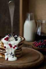 Delicious homemade pancakes, fritters with sour cream and fresh forest berries on rustic wooden background. Selective focus, background
