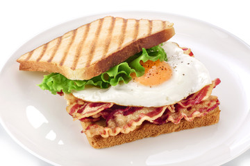 Sandwich with bacon, fried egg and lettuce on a plate.