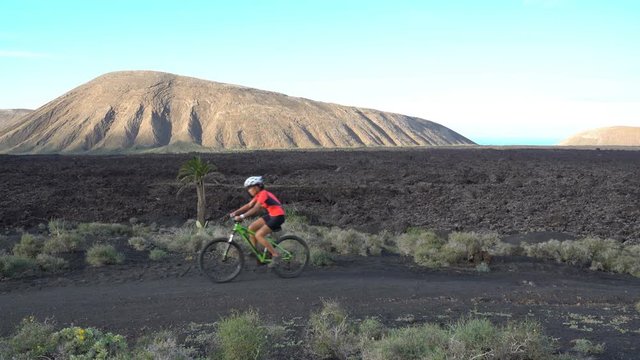 Mountain biking MTB cyclist woman cycling on bike trail path. Female mountain biker on bike in sportswear riding bicycle enjoying healthy active lifestyle in nature, Lanzarote, Canary Islands, Spain