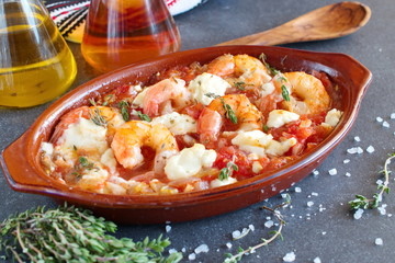 Oven backed prawns with feta, tomato, paprika, thyme in a traditional ceramic form on a abstract background. Healthy eating concept. Mediterranian lifestyle.