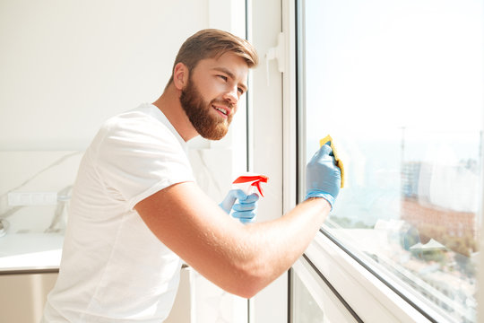Side view of smiling bearded man wipes a window
