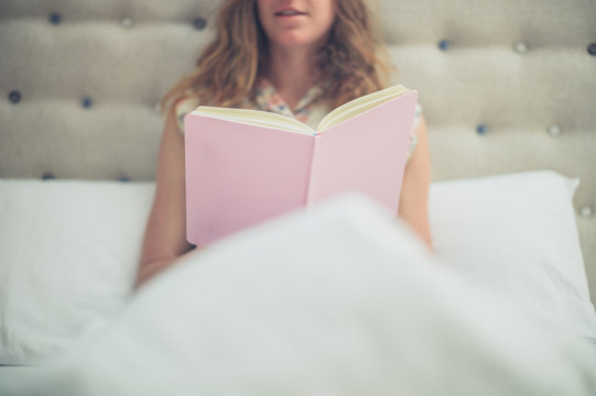 Woman reading pink book in bed