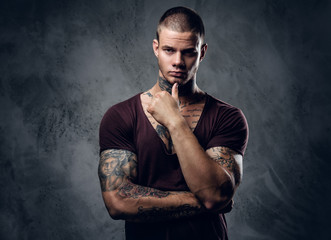 Tattooed male with crossed arms over grey background.