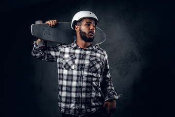 A man holds long board over grey background in a studio.