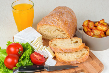 Breakfast from bread, cheese, tomatoes, potatoes and all-over salad on a wooden table closeup.