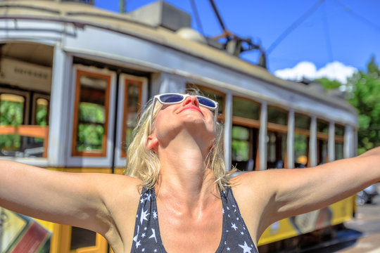 Happy woman with open arms in Lisbon, Portugal, Europe. Blonde caucasian female enjoying the historic tram line, icon of Portuguese capital.Yellow vintage tram on background.Travel and tourism concept