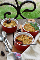 Fruits casserole or crumble with apples and berries in brown cup ramekin on wooden background. Copy space. Photographing with natural light