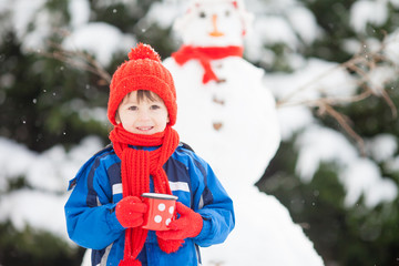 Happy beautiful child building snowman in garden