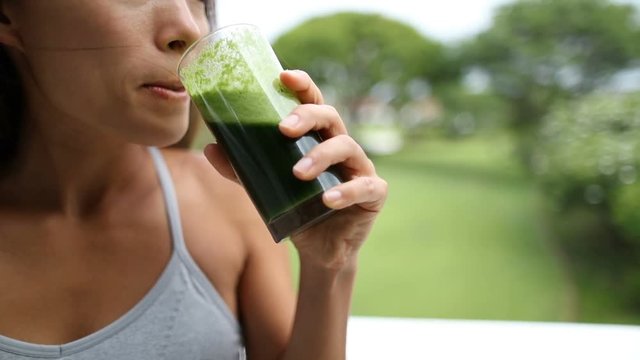 Happy young woman drinking fresh green juice enjoying detox cleanse. Fit female is enjoying healthy drink at park.