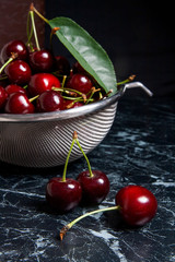 Several red sweet cherries and big green leaf on the table. Fresh organic cherry in colander on dark marble background..