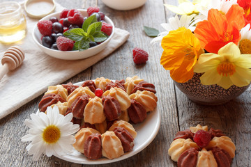 Biscuit with fresh berries on white plate and garden flowers on wooden background. Selective focus.
