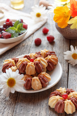 Biscuit with fresh berries on white plate and garden flowers on wooden background. Selective focus.