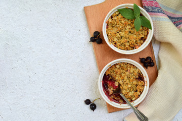 Fruits casserole or crumble with apples and berries in brown cup ramekin on light background. Copy space. Photographing with natural light