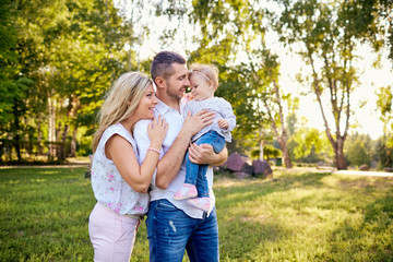 Happy family in a park in summer autumn. Mother, father and baby play in nature in the rays of sunset.