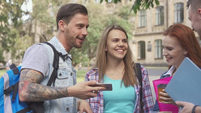 Attractive caucasian students meeting on campus. Two handsome guys highfiving on the walkway outdoors. Close up of two couple of young people watching some images on smartphone