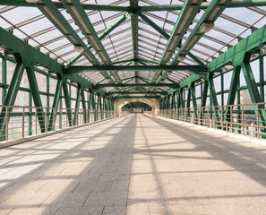 Inside view of long green metal crosswalk bridge with transparent roof