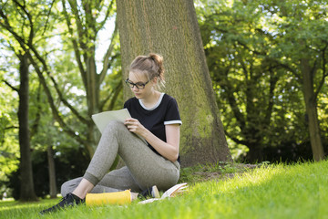 Eine junge Frau sitzt unter einem Baum und schreibt in einem Heft