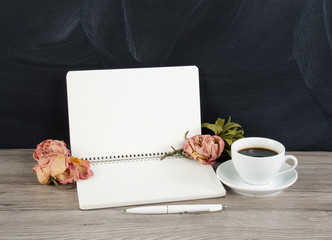 Blank opened notepad with copyspace, cup of coffee and roses on wooden background.