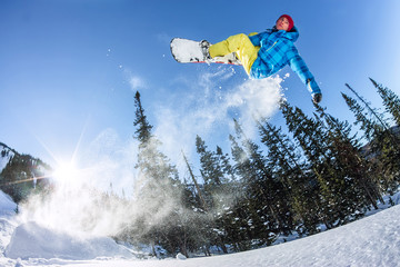 Snowboarder freerider jumping from a snow ramp in the sun on a background of forest and mountains