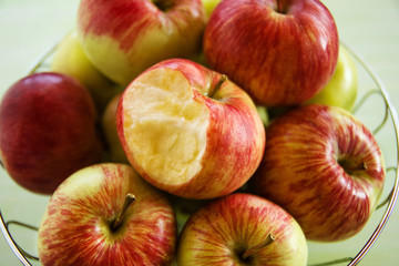 Metal bowl with green, yellow and red apples and one bitten apple closeup, top view.