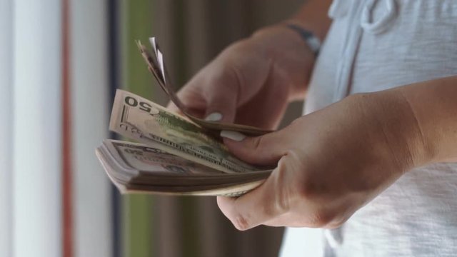 Close-up side view of hands of female counting cash money.