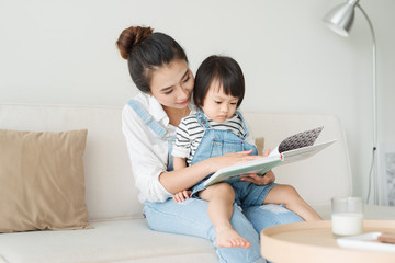 Happy loving family. Pretty young asian mother reading a book to her daughter - Powered by Adobe