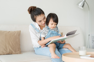 Happy loving family. Pretty young asian mother reading a book to her daughter