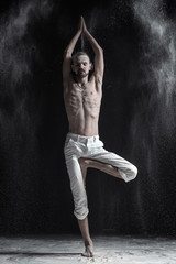 Portrait of caucasian young man wearing white sport pants doing yoga or pilates exercise.