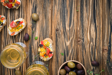 Traditional Italian appetizer, bruschetta with cottage cheese, cherry tomatoes, pepper, olives and fresh thyme, served with wine. Healthy snack concept on wooden rustic table. Top view, copy space