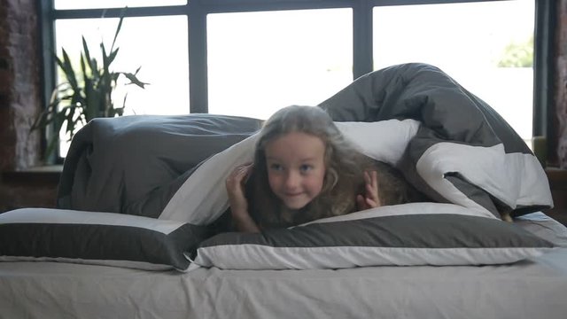 Smiling happy family posing under duvet in bedroom