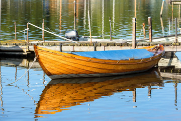 Wooden motorboat with blue tarp moored in calm and windless water by an old pier.