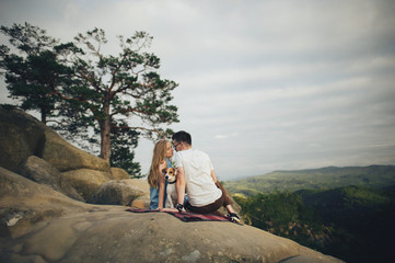 Fototapeta premium Young couple in love resting on peak of mountain in summer. Couple spreading a blanket for picnic