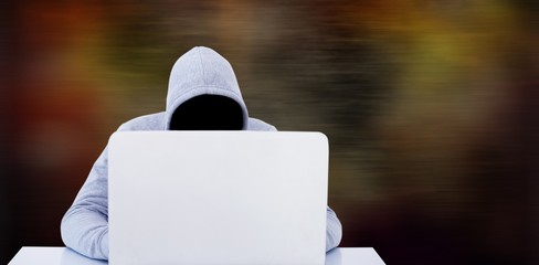 Composite image of hacker using white laptop at table