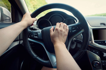 Naklejka premium Close up of woman hand pressing the horn button while driving a car through the road. Woman driving a car with hand on horn button. Closeup woman hand holding steering wheel and honking the horn