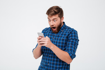 Shocked bearded man in checkered shirt writing message on smartphone