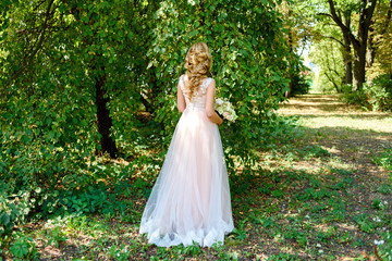 Obraz na płótnie Canvas Beautiful bride in long wedding dress with bridal bouquet of flowers walking in the park outdoor. Happy bride in wedding dress on summer day, free space