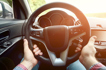 Close up of steering wheel in male driver hands, toned. Man's hands holding steering wheel inside...