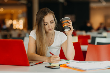 pretty female student with laptop and coffee learning in a high school library