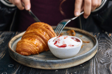 Girl drink coffee, and eat croissant with ice-cream and pink strawberry jam on black wooden table. Tasty background. Hands hold the fork and knife.