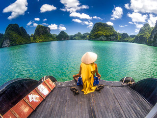 man wearing a Vietnamese hat enjoying the magnifiecent sight of Ha Long bay limestone rocks on a beautiful sunny day during a boat cruise, Vietnam