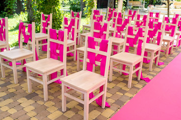 Wedding chairs on each side of archway with pink cloth. Place for wedding ceremony decorated in pink color,  wooden chairs for guests outdoors. Wedding ceremony in pink color