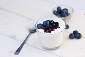 Fototapeta na wymiar Glass cup of yogurt with blueberries on white table and white background